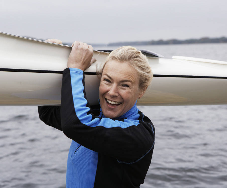 Vrouw staat met kano op haar schouder aan de waterkant