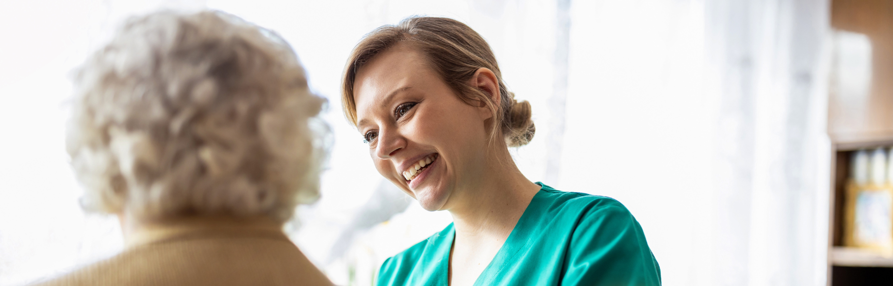 verzorgende kijkt lachend naar oudere vrouw