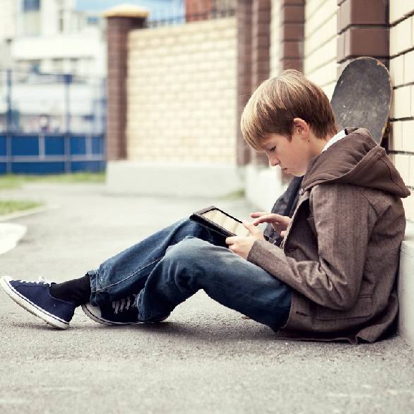 Tiener zit buiten op de grond op tablet met skateboard
