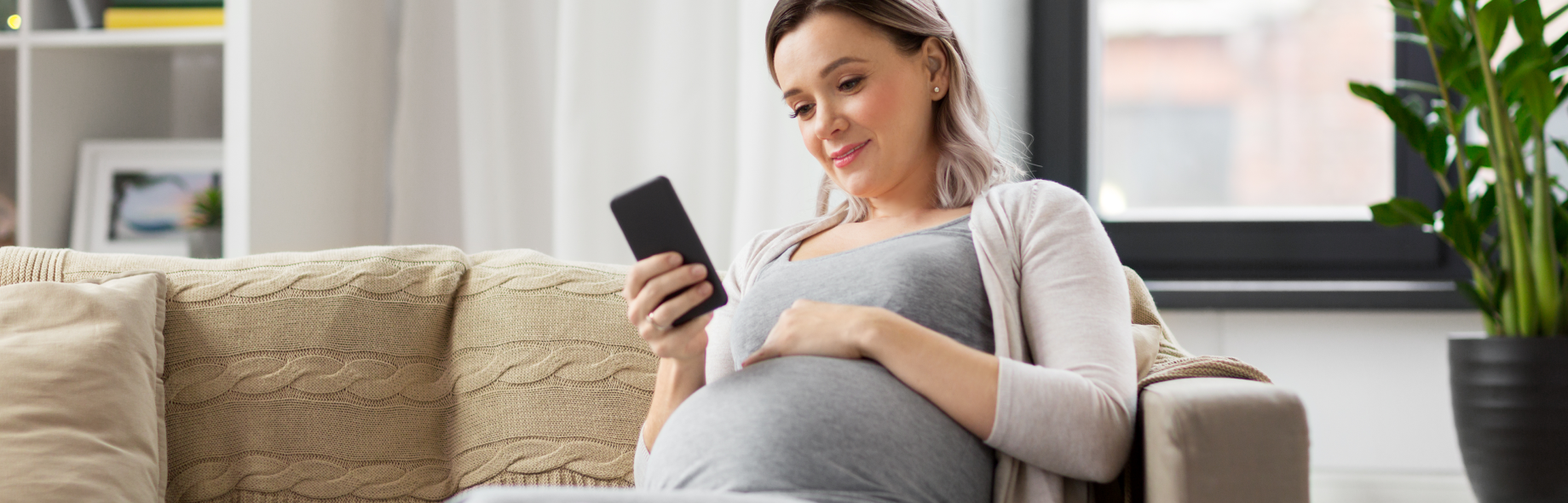 zwangere vrouw met telefoon in haar hand op de bank