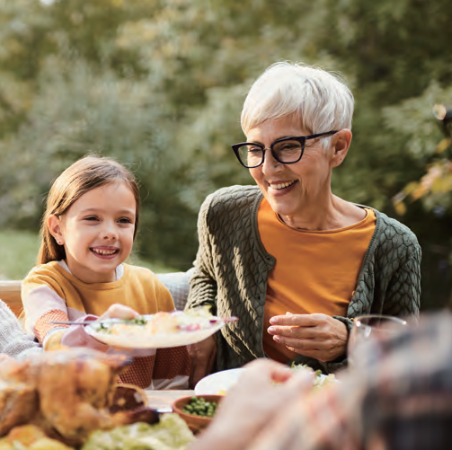 Vrouw op leeftijd en jong meisje zitten lachend aan een tafel met eten