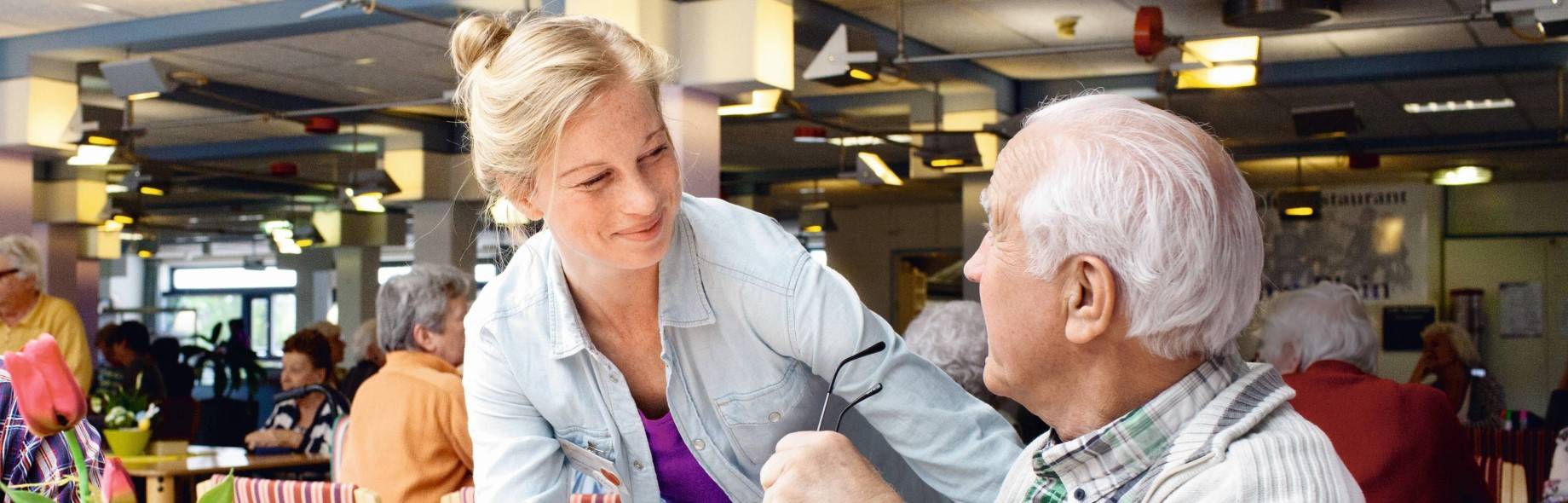 vrouw helpt man in gezamenlijke ruimte zorginstelling